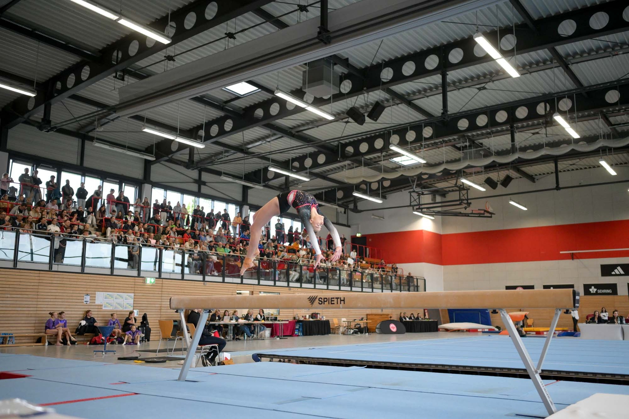 Turnen am Schwebebalken, dahinter die Halle zu erkennen