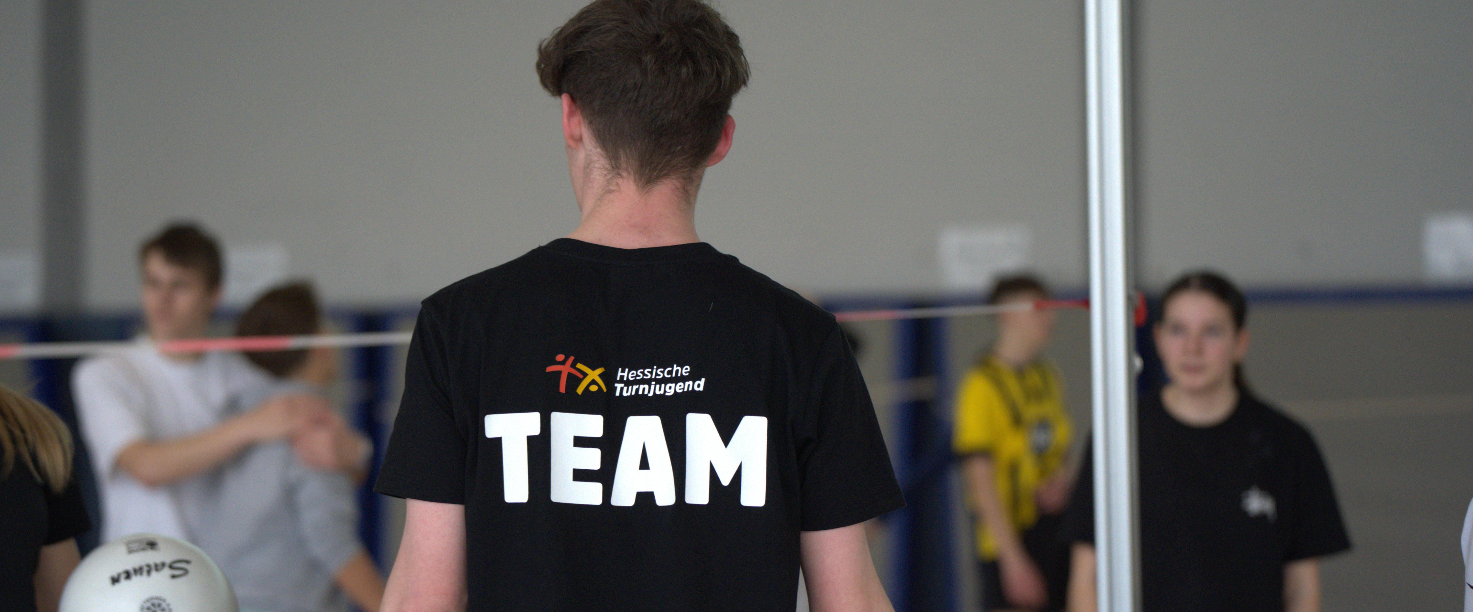 Es ist der Rücken eines Trainers zu sehen, auf dessen T-Shirt Team geschrieben steht.