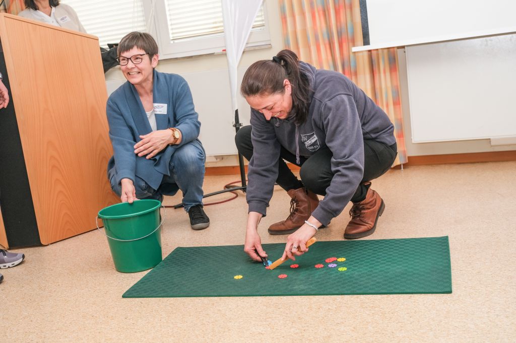 Zwei Frauen hocken auf dem Boden und spielen mit kleinen bunten Plättchen.
