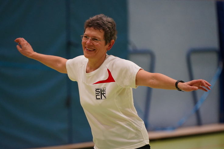 Eine ältere Frau macht eine Bewegung und lacht.