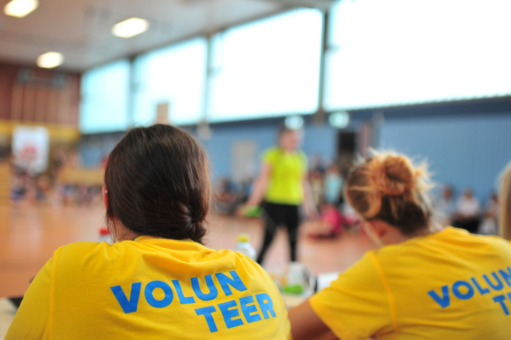 Mehrere Personen sitzen in einem gelben Volunteer-Shirt an einem Tisch.