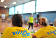 Mehrere Personen sitzen in einem gelben Volunteer-Shirt an einem Tisch.