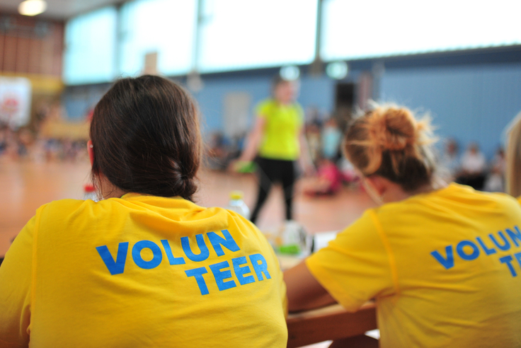 Mehrere Personen sitzen in einem gelben Volunteer-Shirt an einem Tisch.