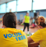 Mehrere Personen sitzen in einem gelben Volunteer-Shirt an einem Tisch.
