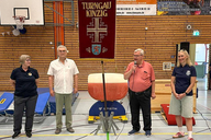 4 Personen stehen neben der Fahne des Turngaus. Tobias Weisbecker spricht dabei in ein Mikrofon.