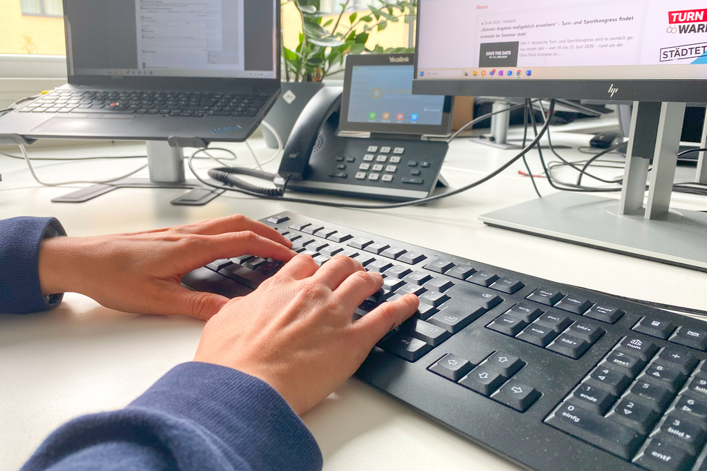 Eine Person sitzt am Schreibtisch im Büro und tippt auf der Tastatur.