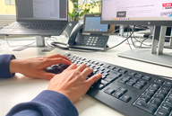 Eine Person sitzt am Schreibtisch im Büro und tippt auf der Tastatur.