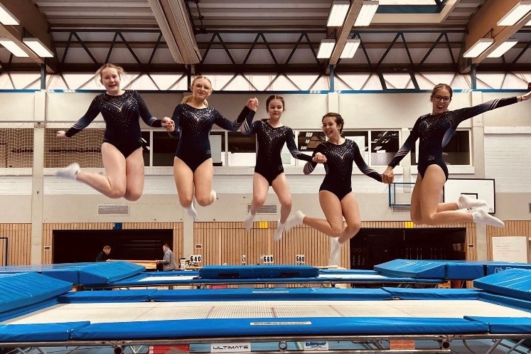 5 Turnerinnen springen auf einem Trampolin in die Luft.