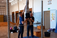 Zwei Männer helfen einer Teilnehmerin am Reck bei einer Übung.