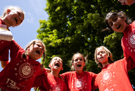 Kinder stehen in einem Kreis, legen die Arme umeinander und rufen einen gemeinsamen Spruch.