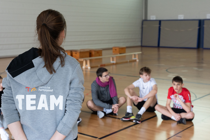 Eine junge Frau erklärt Schülern etwas in der Sporthalle.