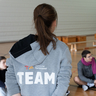 Eine junge Frau erklärt Schülern etwas in der Sporthalle.
