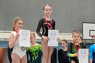 Drei Turnerinnen stehen auf einem Podest.