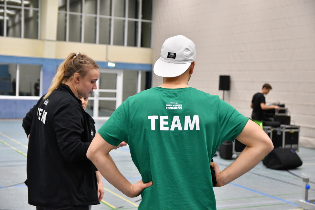 Ein Mann steht in einer Sportgalle und träft die Rückenaufschrift "TEAM".