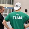 Ein Mann steht in einer Sportgalle und träft die Rückenaufschrift "TEAM".