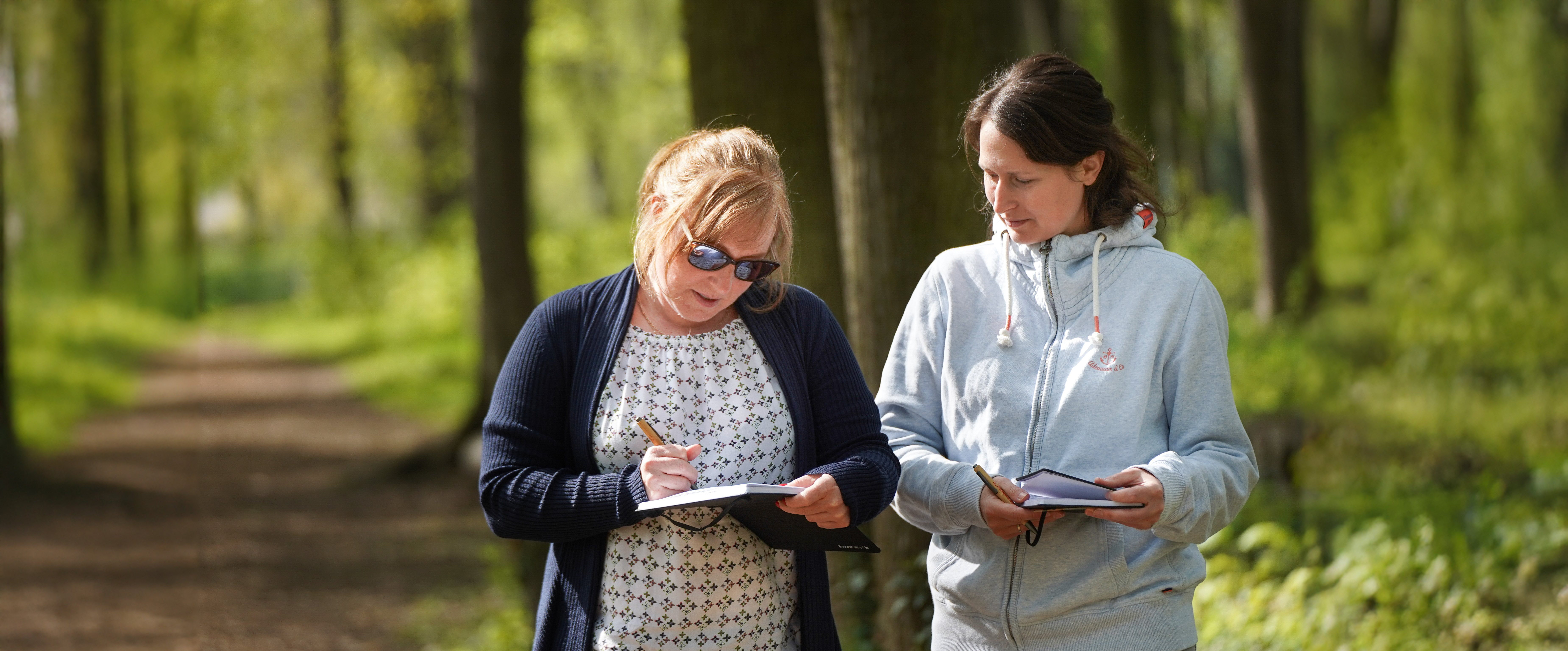 Zwei Frauen laufen auf einem Waldweg und besprechen sich. 