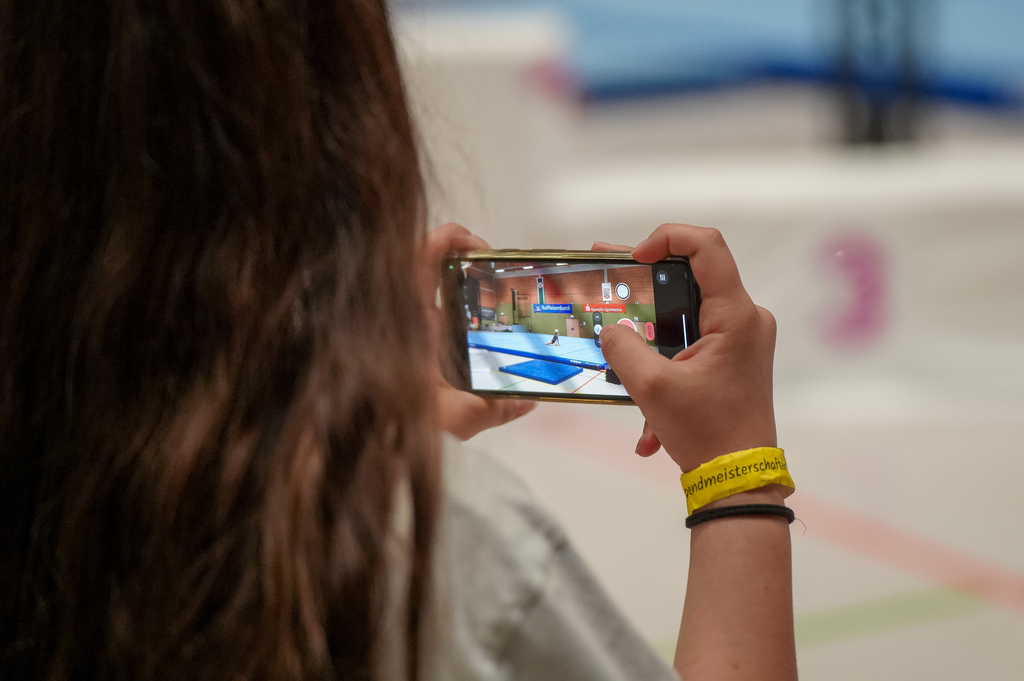 Ein Mädchen filmt eine Szene mit dem Smartphone in der Turnhalle.