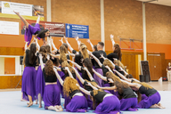 Eine Showgruppe in lila Hosen und schwarzen T-Shirts zeigt eine Endpose.