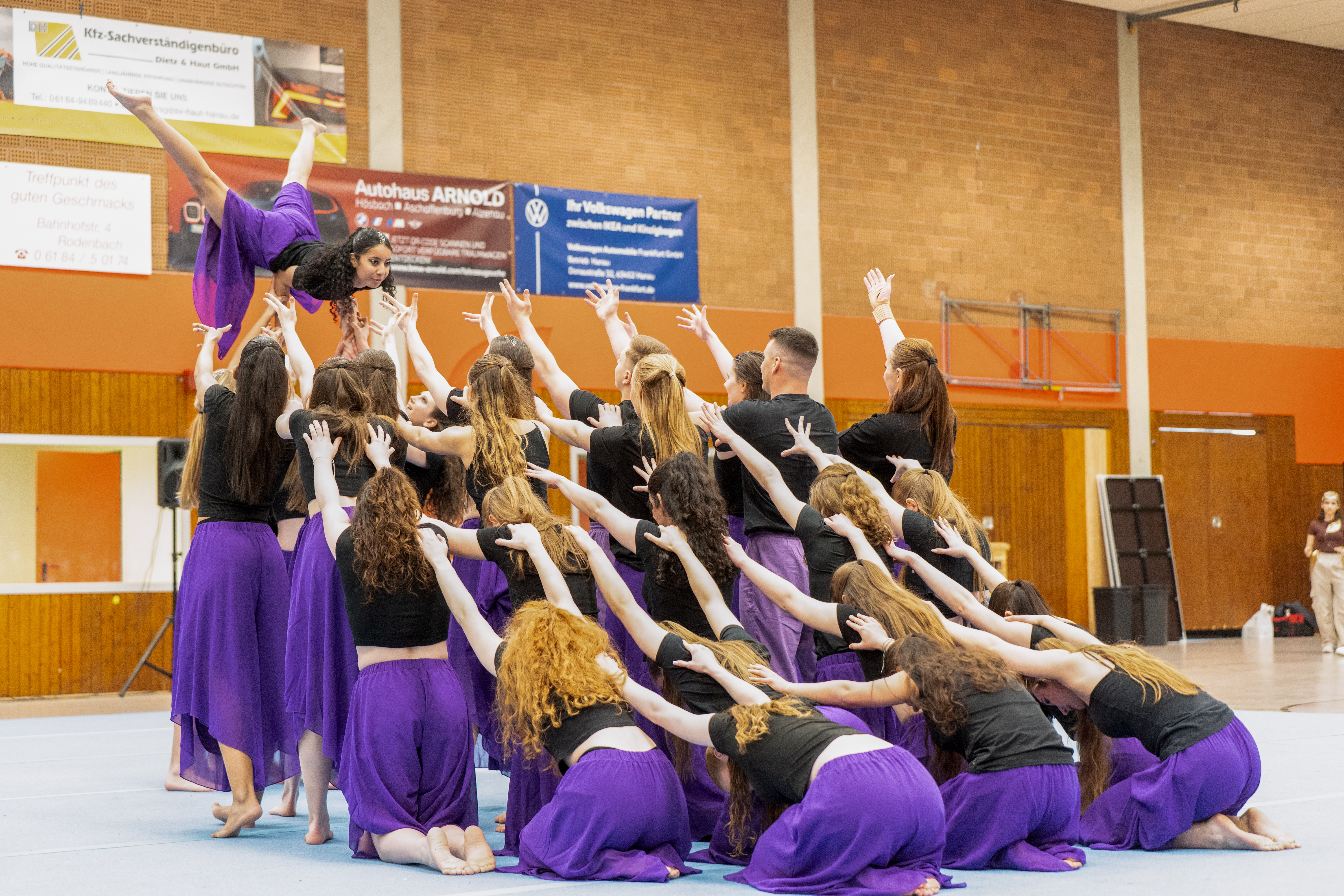 Eine Showgruppe in lila Hosen und schwarzen T-Shirts zeigt eine Endpose.