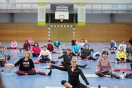 Teilnehmende eines Fitnesskurses sitzen auf ihren Gymnastikmatten und machen eine Übung.