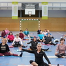 Teilnehmende eines Fitnesskurses sitzen auf ihren Gymnastikmatten und machen eine Übung.