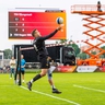 Faustballspieler beim Schlag, im Hintergrund große Leinwand