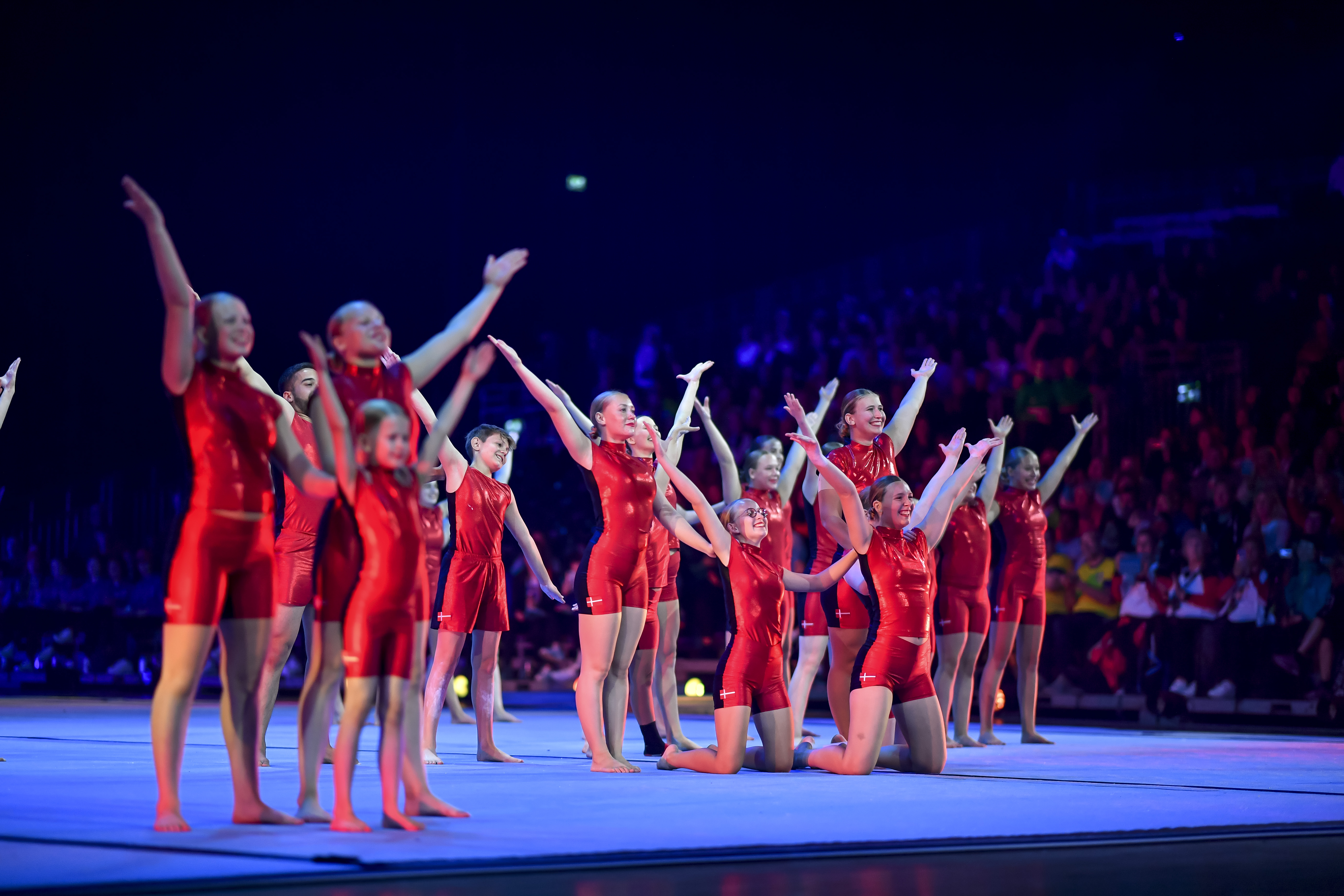 Eine Showgruppe in roten Kostümen zeigt eine Figur auf der Bühne.