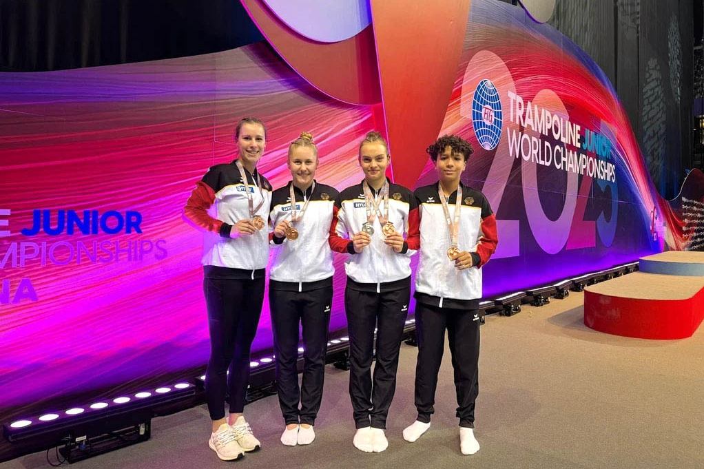 Vier jugendliche stehen neben einander mit ihren Medaillen in der Hand vor der LED-Wand "Trampoline World Championships"