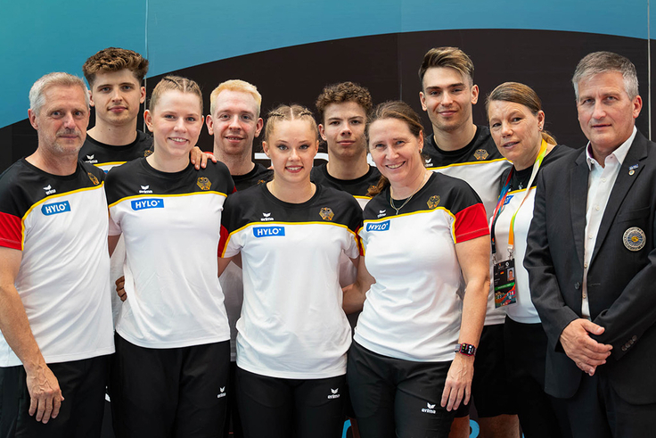 Die Trampolinturner*innen posieren für ein Foto mit ihren Trainer*innen. 