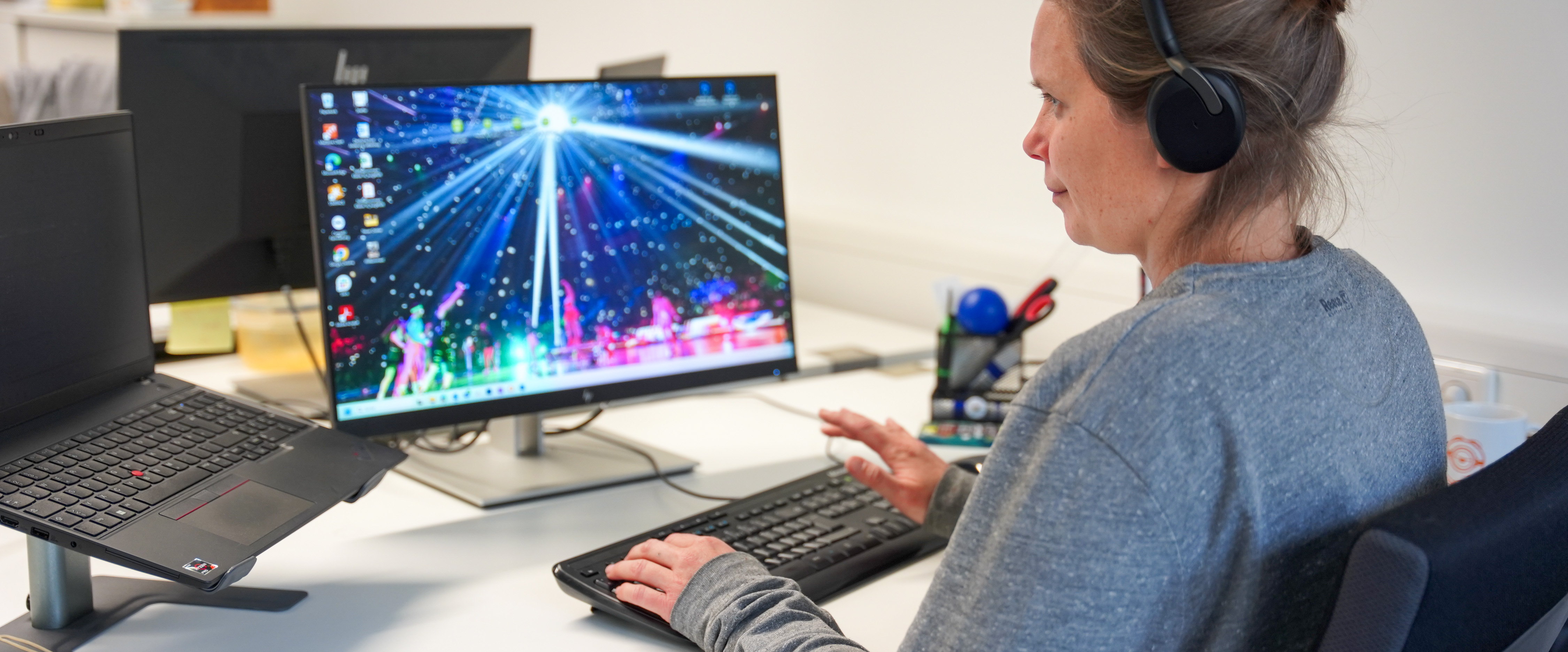 Eine Frau arbeitet an ihrem Laptop und an einem zweiten Bildschirm. Auf dem zweiten Bildschirm ist ein Foto von einer Show zu sehen.