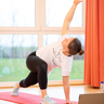 Eine Frau macht eine Mobilisationsübung auf einer Gymnastikmatte, vor ihr steht ein Laptop.