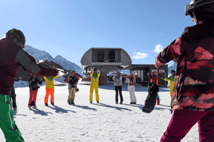 Eine Gruppe von Skifahrer*innen dehnen sich zusammen auf der Piste.