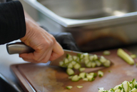 Ein Koch schneidet Gemüse auf einem Brettchen.