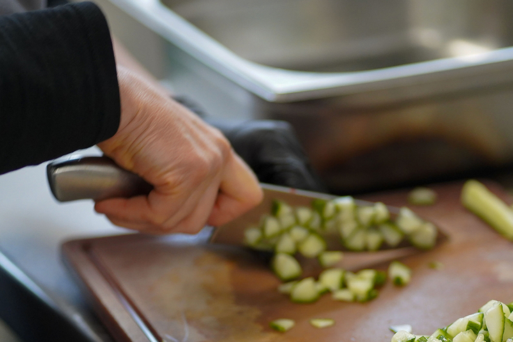 Ein Koch schneidet Gemüse auf einem Brettchen.