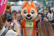 Das neue Maskottchen der HTJ posiert mit zwei jungen Frauen für ein Foto.