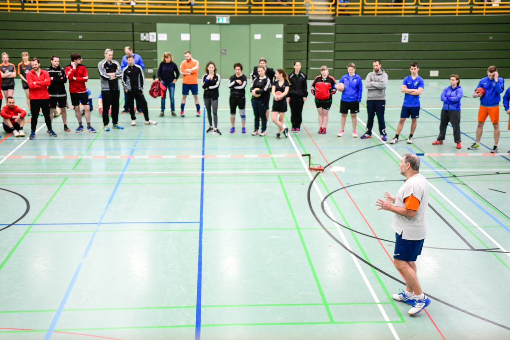 Sportler und Sportlerinnen der Sportart Zweier-Prellball lauschen einem Referierenden in einer Sporthalle.