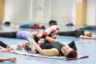 Eine Frau liegt mit dem Rücken auf einer Gymnastikmatte und macht eine Dehnübung.