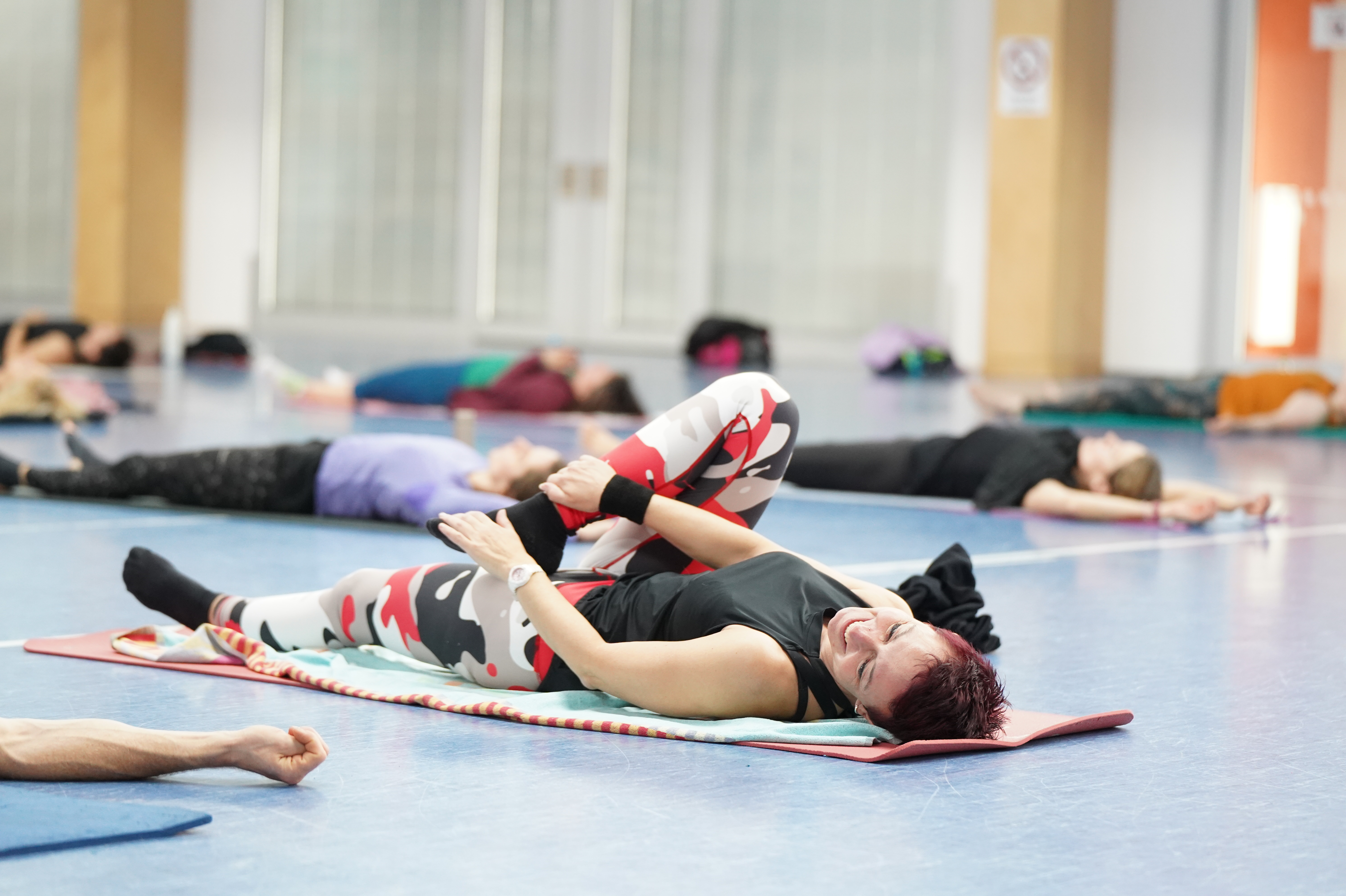 Eine Frau liegt mit dem Rücken auf einer Gymnastikmatte und macht eine Dehnübung.