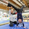 Eine Athletin in der Hocke hält ein Kind beim Handstand.