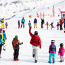 Eine große Gruppe von Skifahrern stehen auf der Schneepiste in einem Kreis und machen gemeinsam Gymnastikübungen.