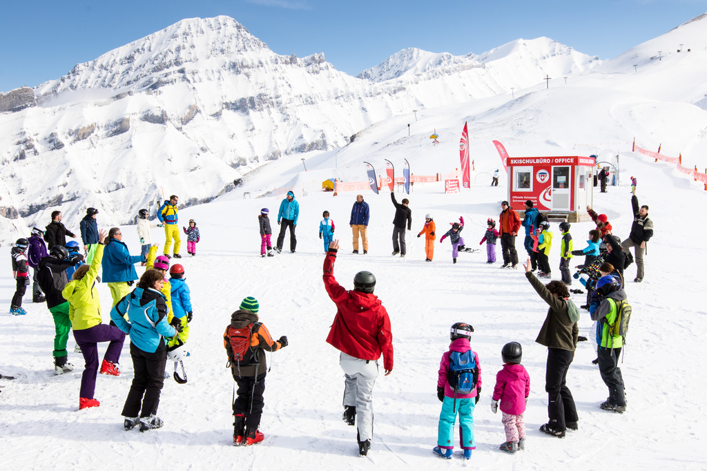 Eine große Gruppe von Skifahrern stehen auf der Schneepiste in einem Kreis und machen gemeinsam Gymnastikübungen.