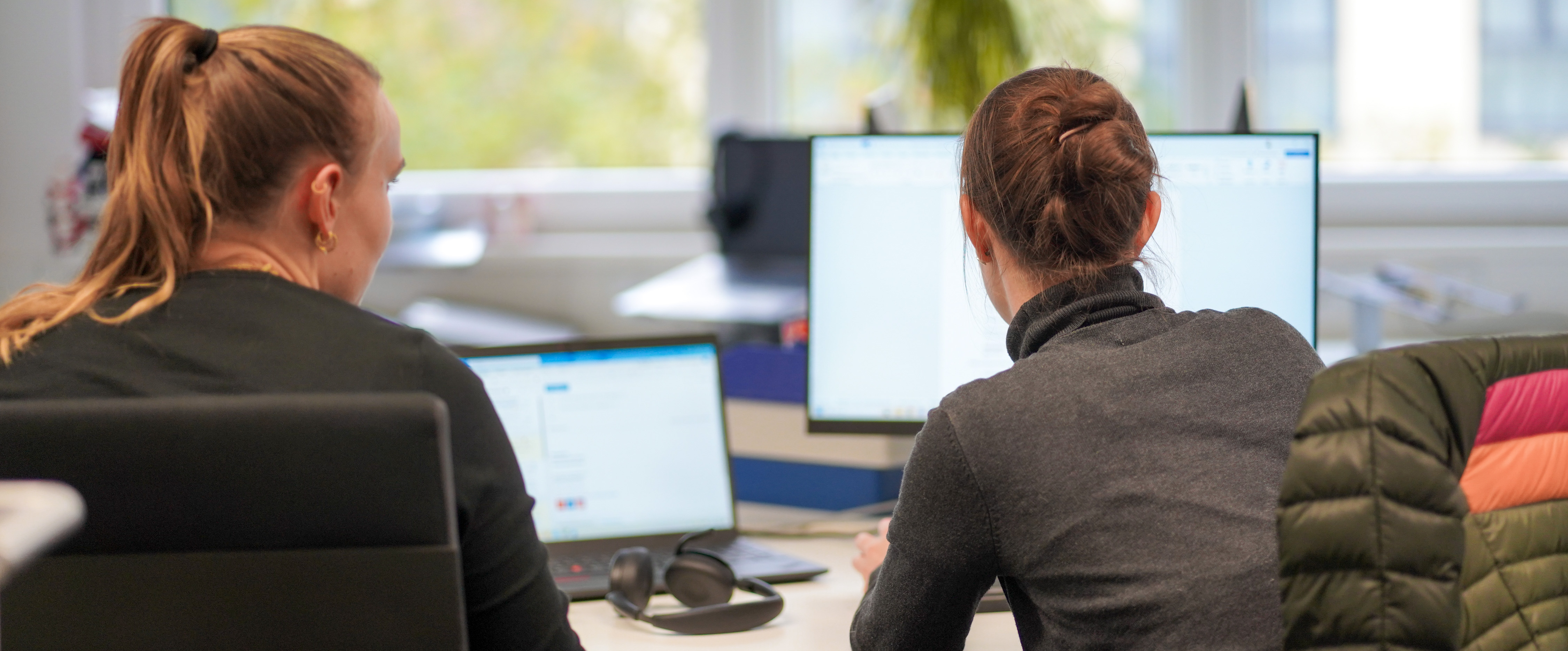 Zwei Personen sitzen zusammen an einem Schreibtisch und arbeiten an Computern..