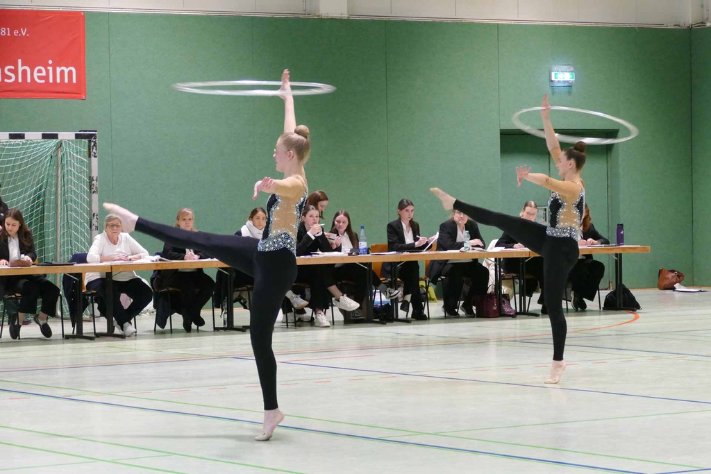 Zwei Gymnastinnen, ein Bein gespreizt in der Luft, mit einem Reifen über den Kopf