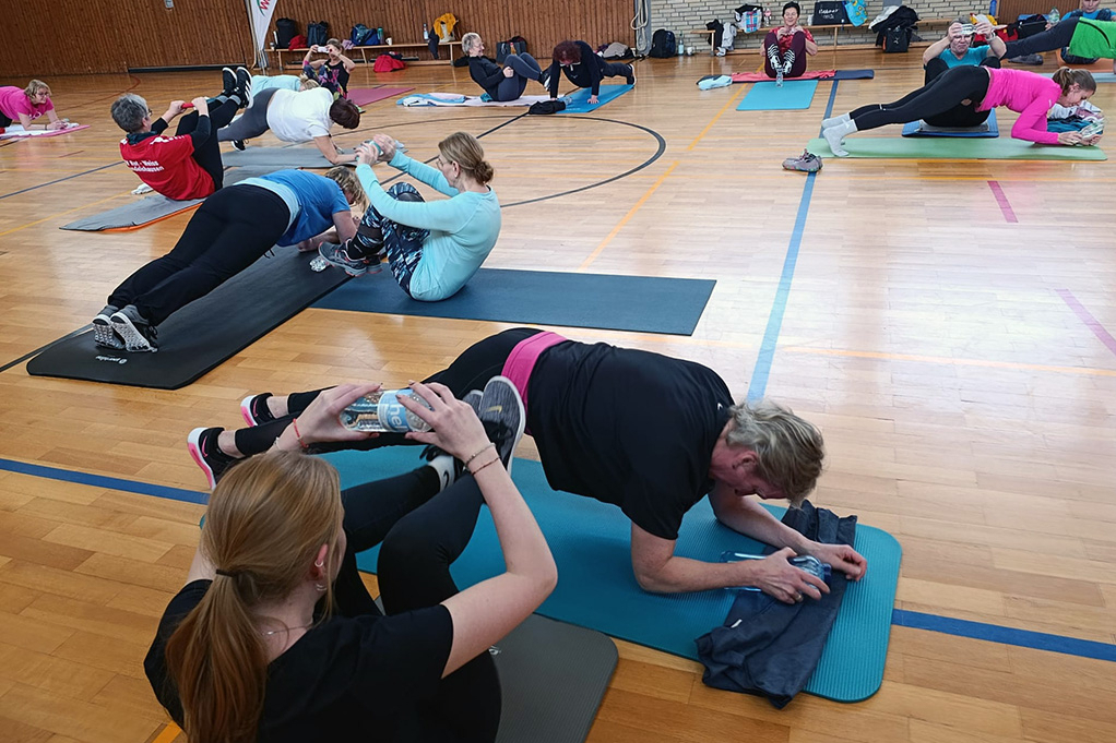 Personen machen Sportübungen auf Matten.