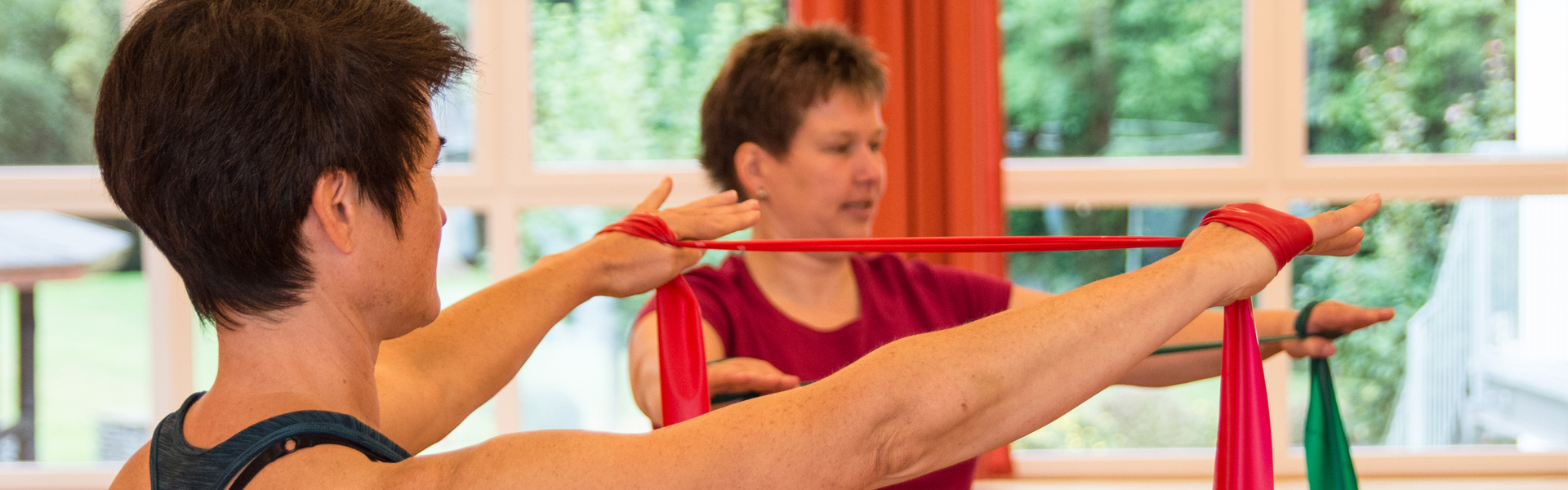 Zwei Frauen zeigen eine Übung mit einem Gymnastikband.