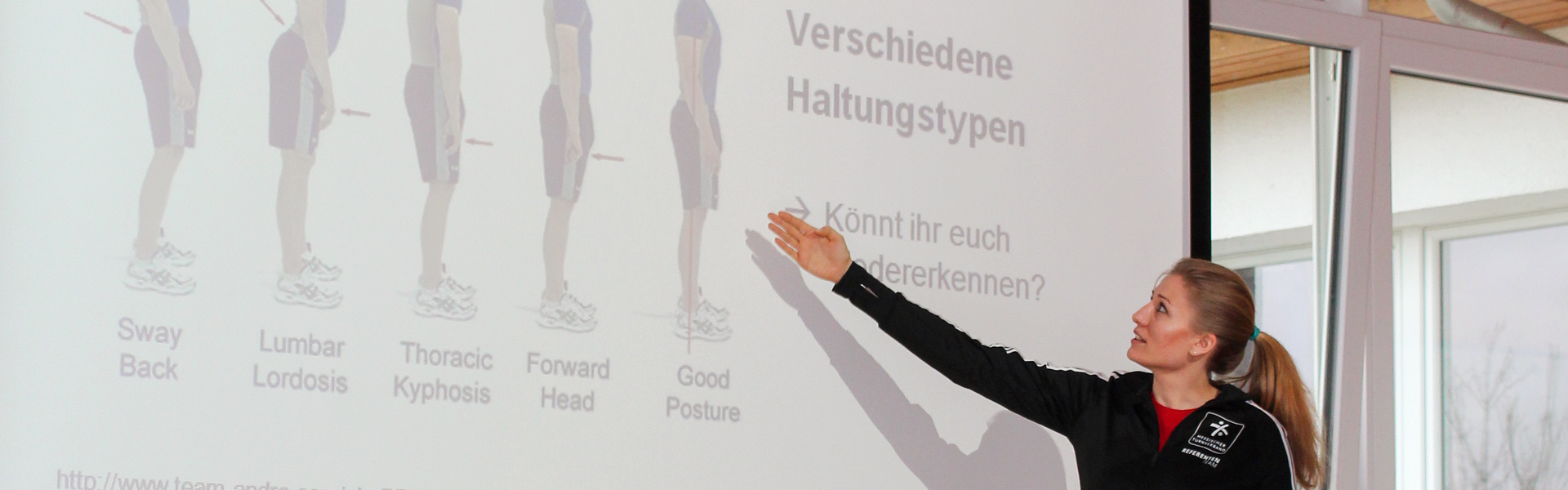 Eine Frau zeigt auf eine weiße Leinwand auf der eine Abbildung gezeigt wird.
