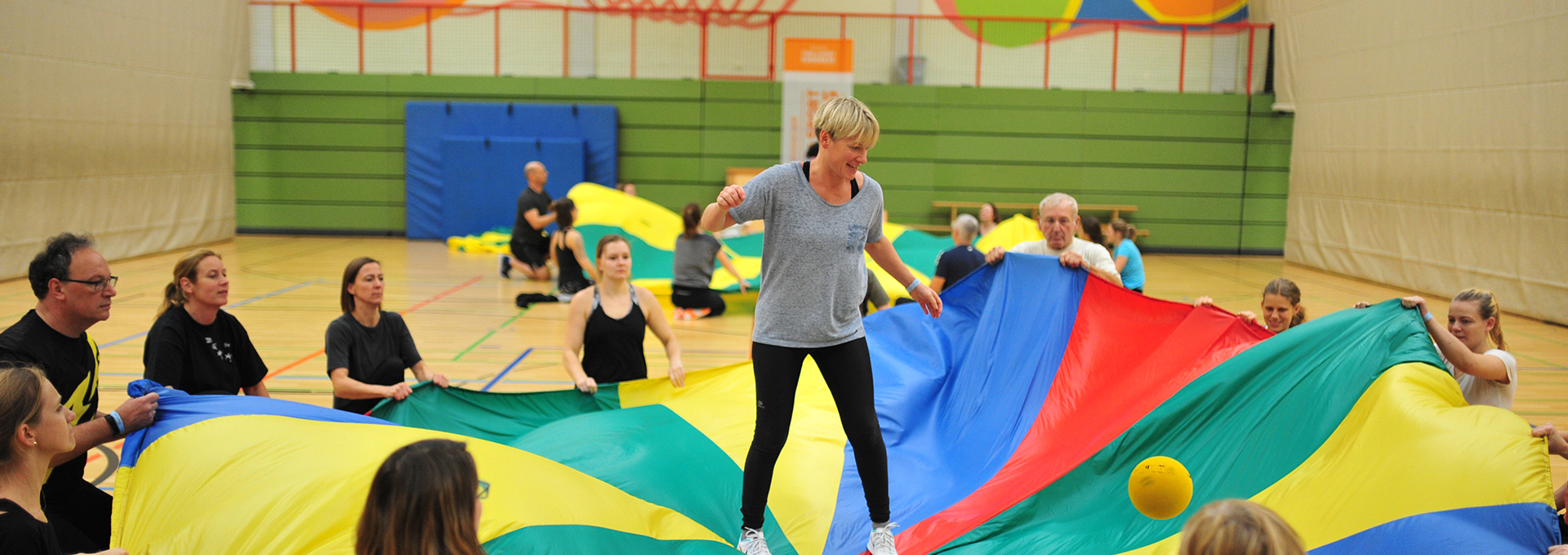Eine Frau spielt gemeinsam auf einem großen bunten Tuch, das von mehreren Personen gehalten wird.