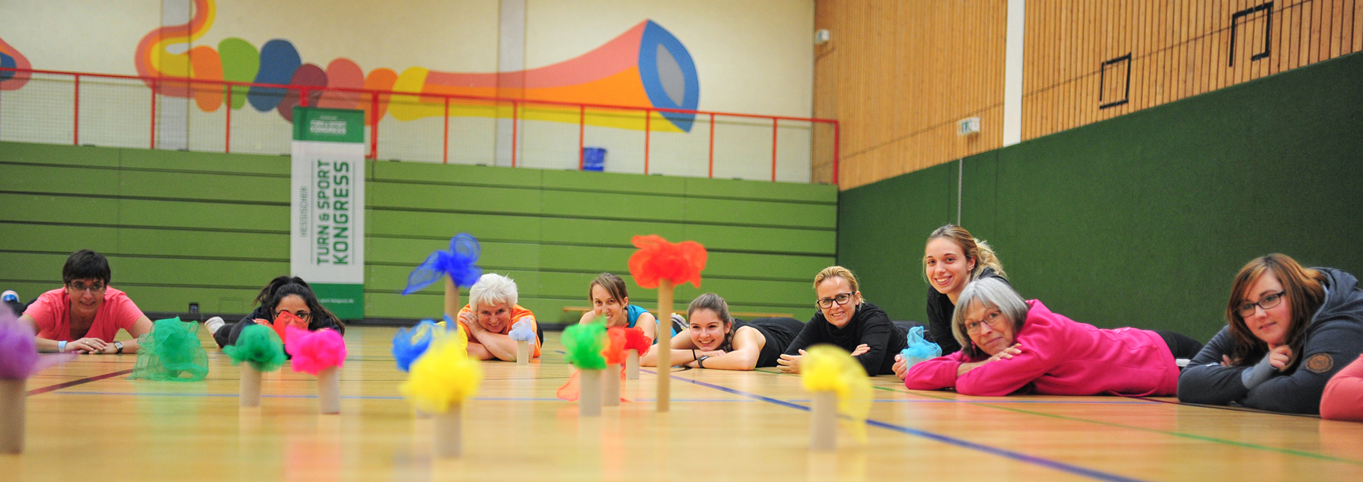 Eine Gruppe Personen liegt in einer Halle auf dem Boden und spielt mit bunten Tüchern.