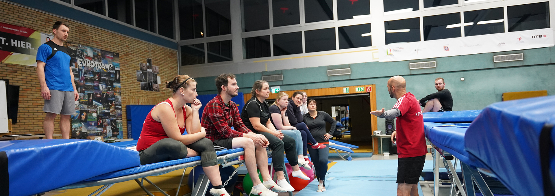 Eine Gruppe von Personen sitzt auf Trampolin und hören dem Referenten zu.