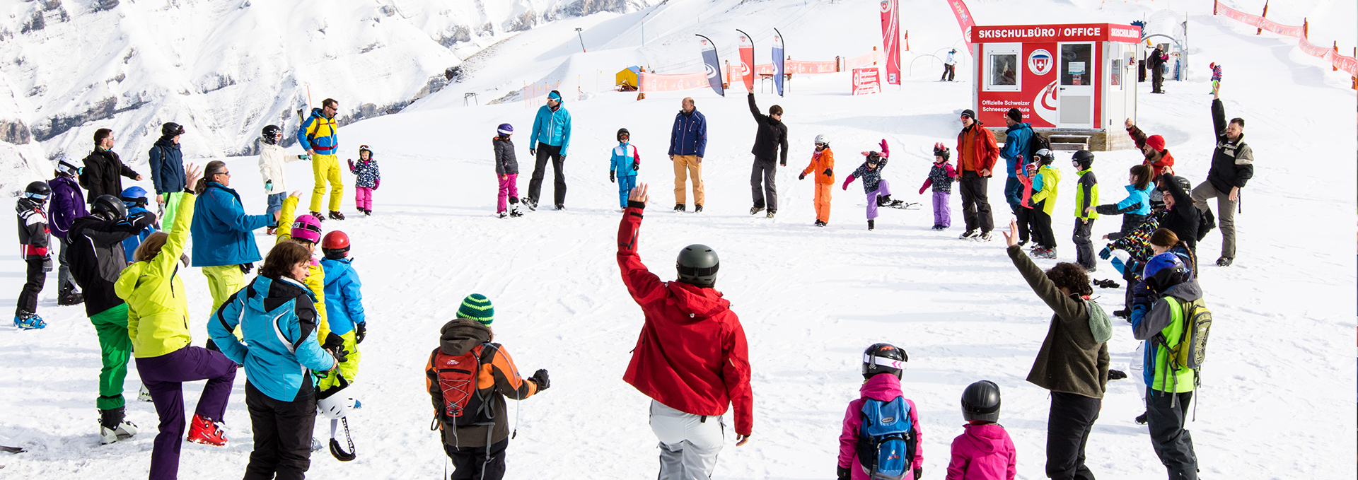 Eine Gruppe von älteren und jungen Wintersportlern stehen im Schnee in einem Kreis zusammen.